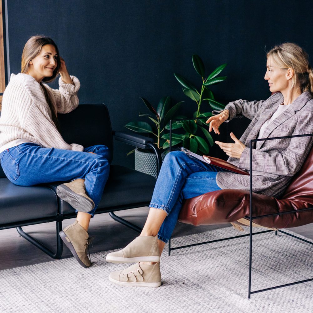 A smiling woman listens to the advice of a consultant psychologist sitting on a sofa in the workshop A smiling woman listens to the advice of a consultant psychologist sitting on a sofa in the workshop.