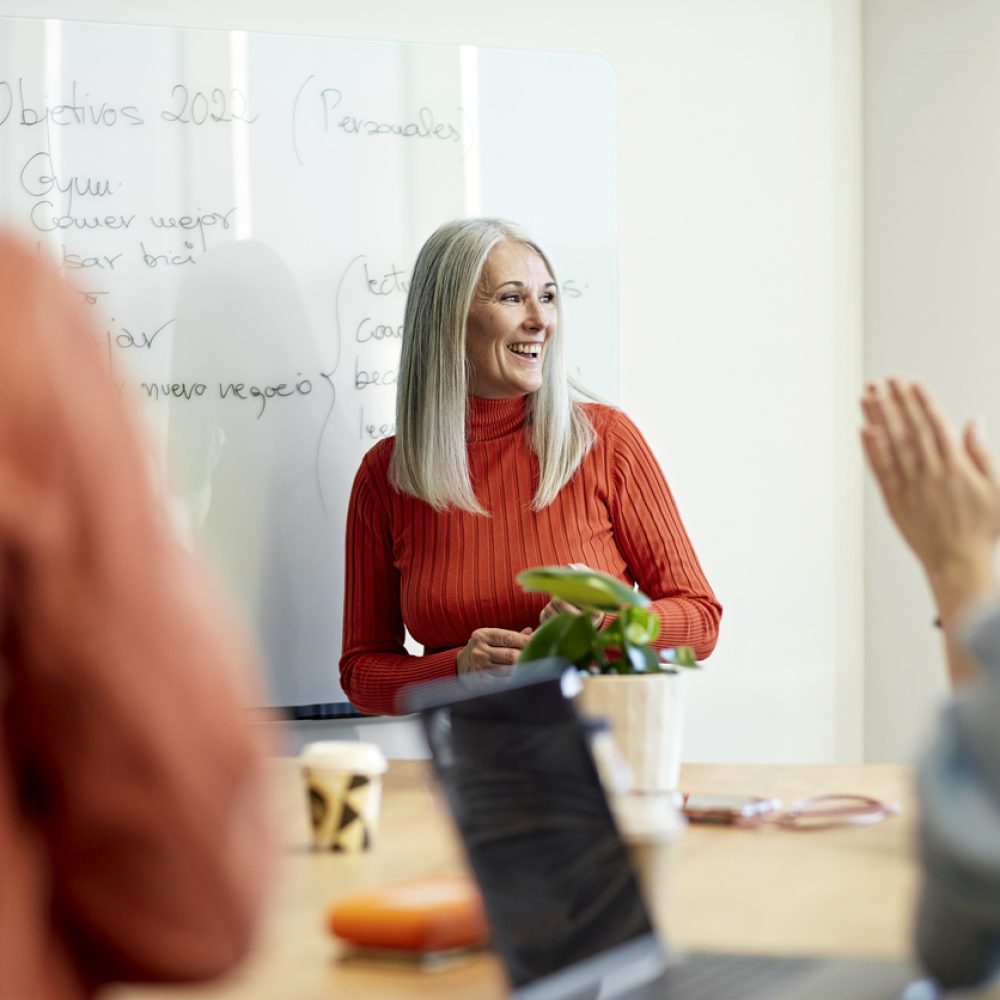 Barcelona businesswoman presenting objectives for new year Personal perspective of mid 50s executive smiling and looking away as she receives applause from colleagues for her ideas at informal meeting.